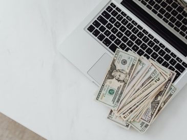 Close-up of US dollar bills scattered on a laptop keyboard on a white desk, symbolizing digital finance. — C&oacute;mo Inicia