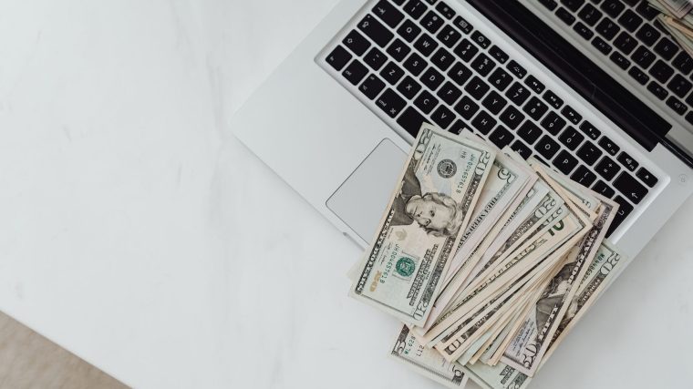 Close-up of US dollar bills scattered on a laptop keyboard on a white desk, symbolizing digital finance. — C&oacute;mo Inicia