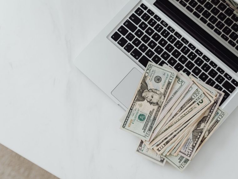 Close-up of US dollar bills scattered on a laptop keyboard on a white desk, symbolizing digital finance. — C&oacute;mo Inicia