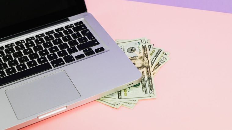 Close-up of a laptop with US dollar bills on a pastel background, symbolizing finance. — Comment Maximiser Votre Exp&eacute;r